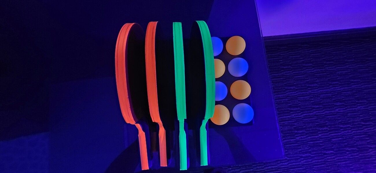 UV table tennis bats and balls glowing orange, green and blue under blacklight