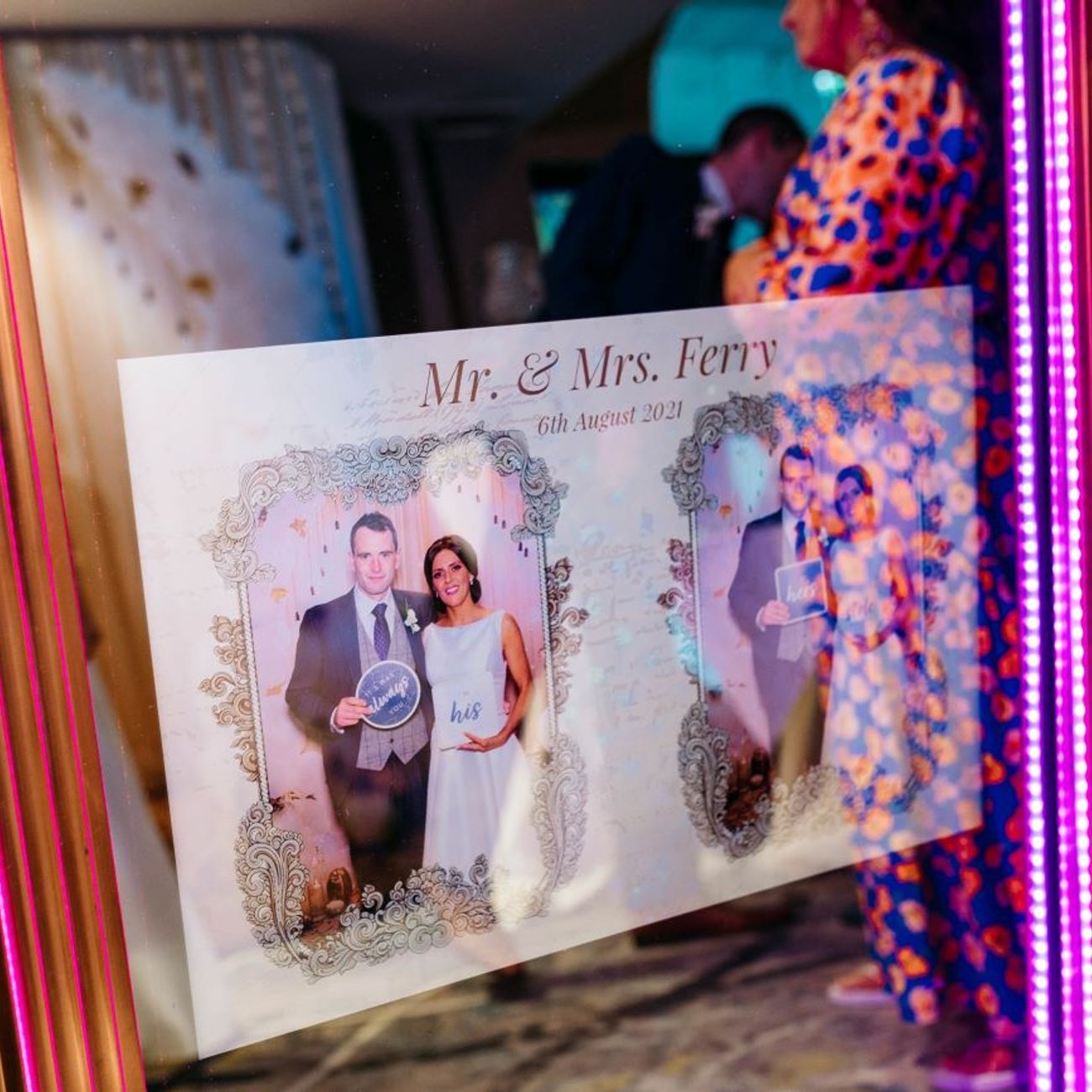 Wedding photo print with a custom 'Mr. & Mrs. Ferry, 6th August 2021' overlay design, held up in front of the magic mirror's pink LED frame