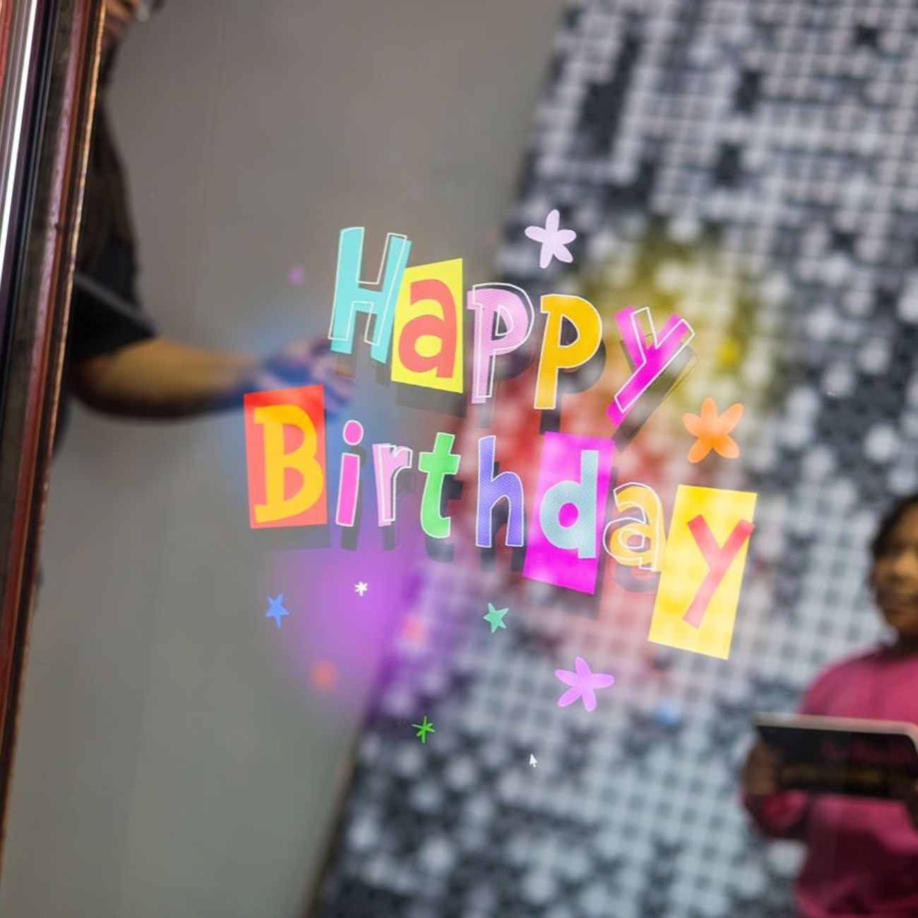 Close-up of the magic mirror's touchscreen showing a colourful animated 'Happy Birthday' overlay, gold mirror frame around the edge with a child reflected at the side