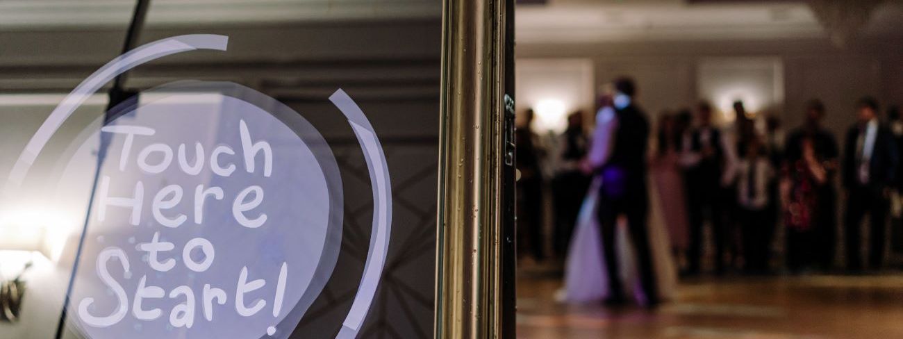 A magic mirror photo booth showing a touch to start screen on a wedding dance floor