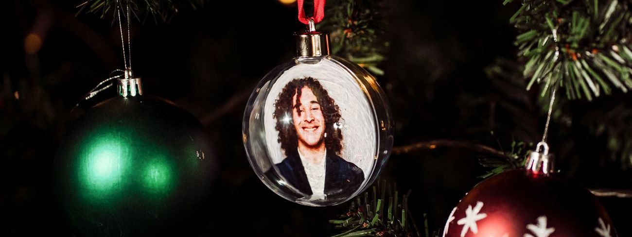 A clear photo bauble with a guest portrait inside, hanging on a Christmas tree between a green bauble and a red snowflake bauble