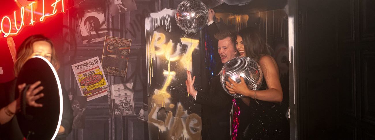 A roaming photo booth in front of a neon disco-ball backdrop at a party