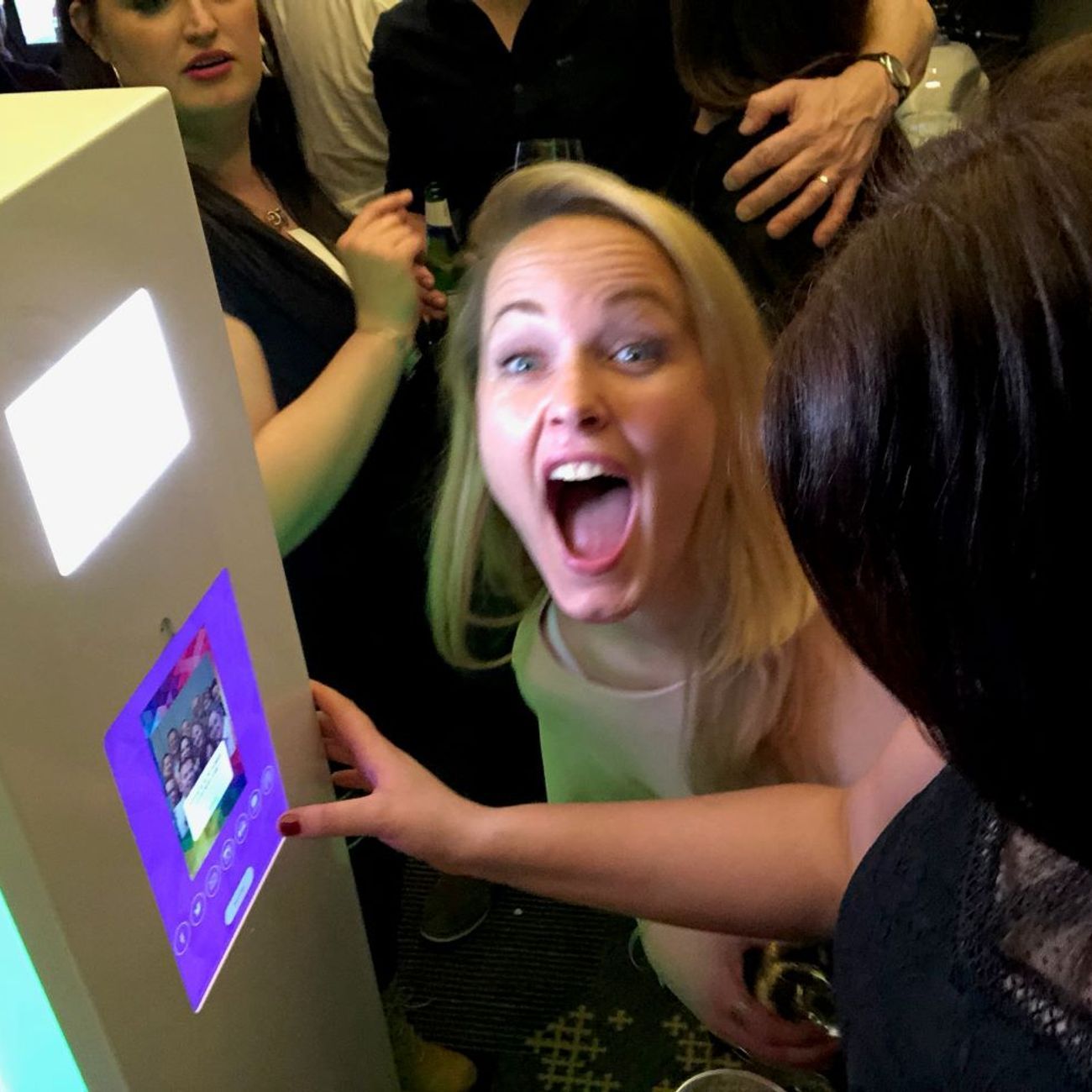Wedding guest laughing with delight at the selfie pod touchscreen as the group preview shows on screen