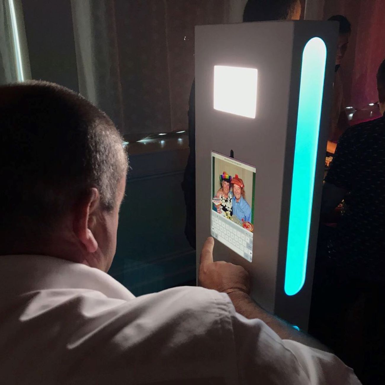 Guest tapping their email address into the selfie pod touchscreen to share a captured photo, with the fill light and LED strip illuminated