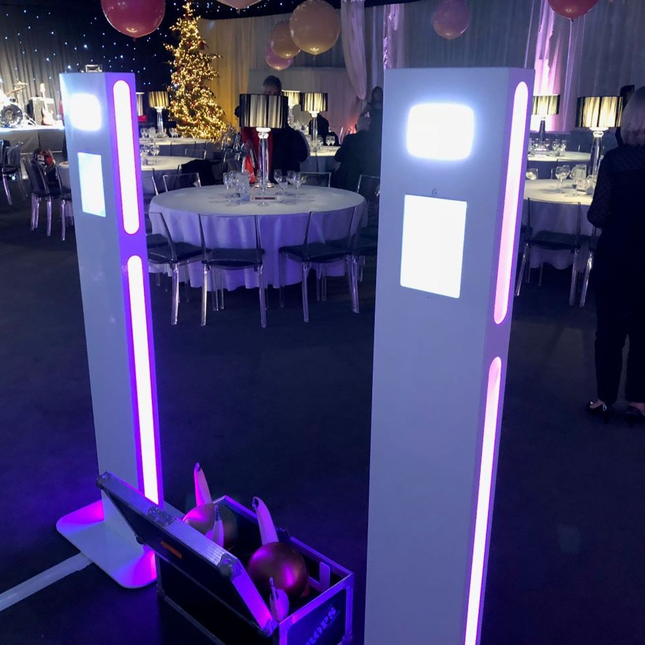 Two selfie pods set up side by side at a corporate Christmas dinner, Christmas tree and round dining tables in the background