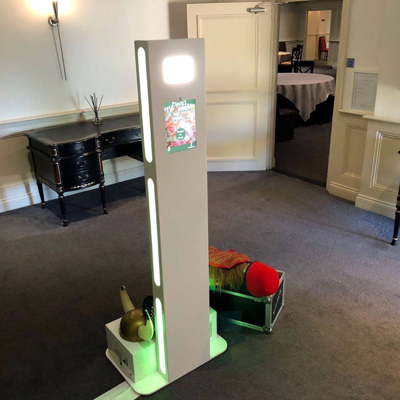 Selfie pod set up in a hotel wedding venue with a couple's poster on the front, props case beside it