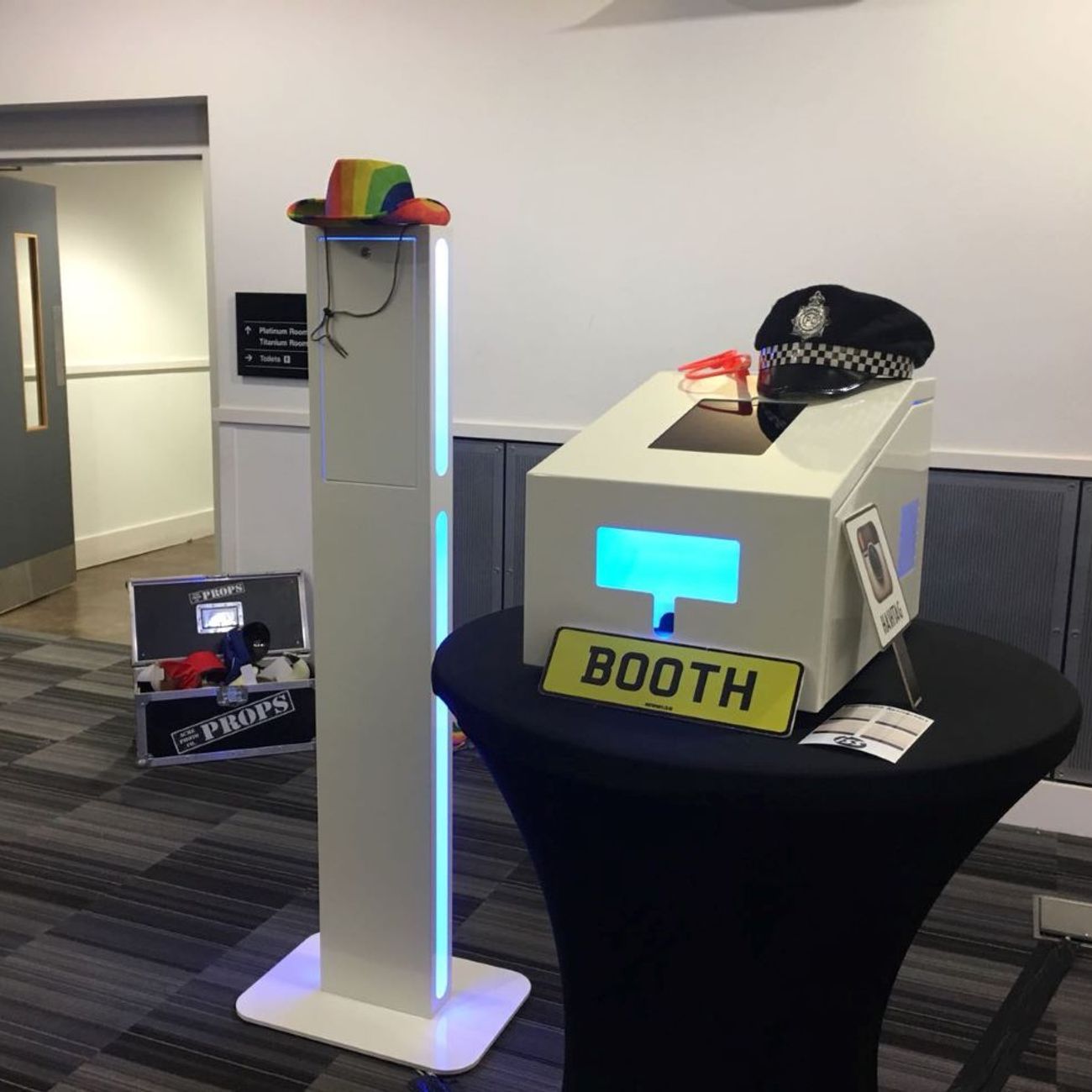 Selfie pod paired with an audio guestbook at a conference venue, props case behind and BOOTH licence-plate prop in the foreground
