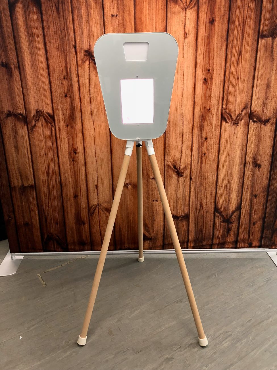 Reverse view of the retro pod on its wooden tripod against a dark wood-panelled wall, showing the white back of the screen housing