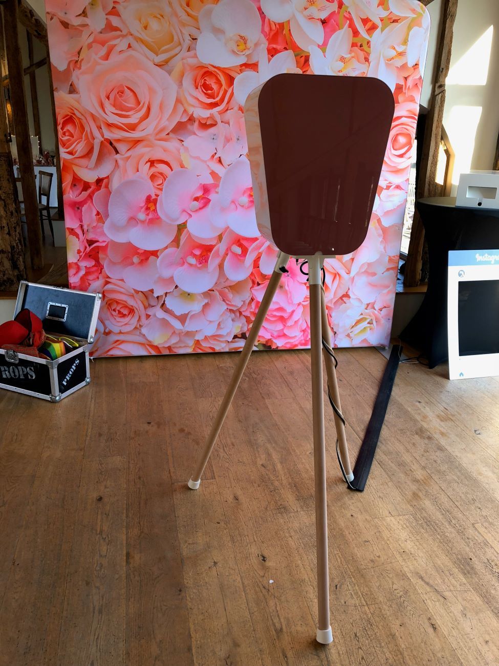 Back-of-fascia view of the retro pod next to a pink-and-white flower wall backdrop, with the props case visible to the side