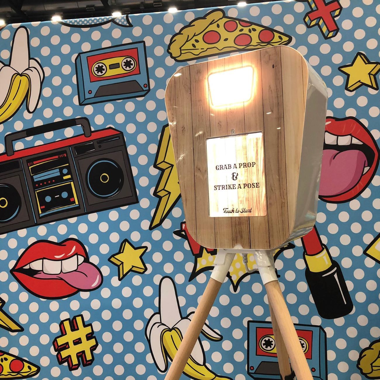Retro pod tripod against a pop-art comic-style backdrop with banana, cassette tape, lipstick, boombox, hashtag and tongue motifs in primary colours