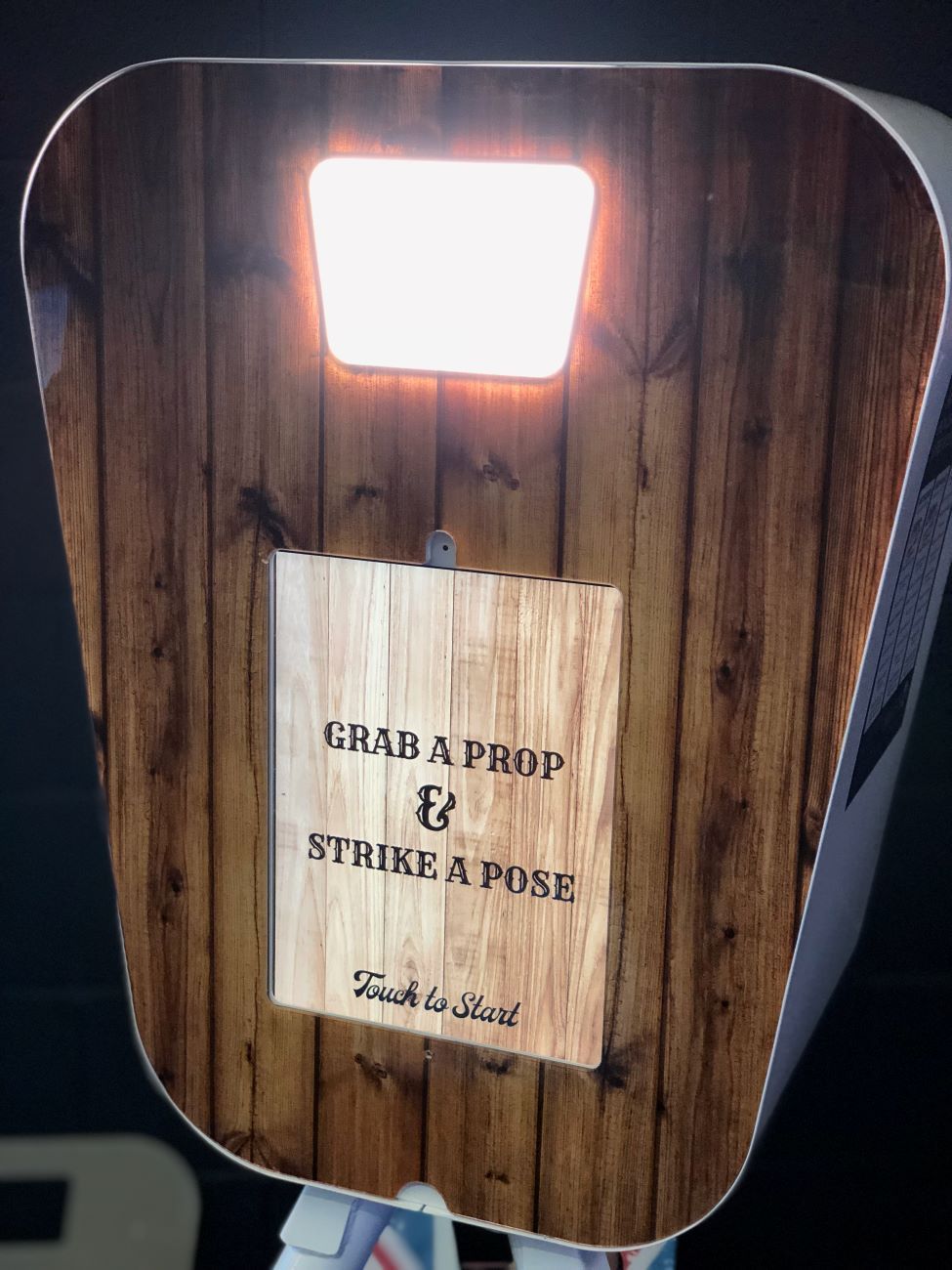 Tight detail of the retro pod's wood-grain fascia — fill-light panel at the top, central wood-pattern screen reading 'Grab a Prop & Strike a Pose / Touch to Start'