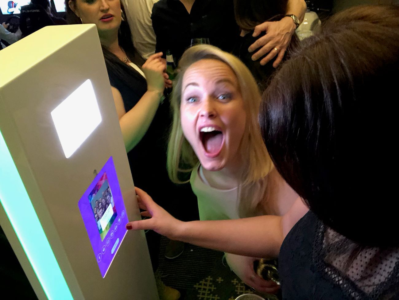 Wedding guest laughing with delight at the selfie pod touchscreen as the group preview shows on screen