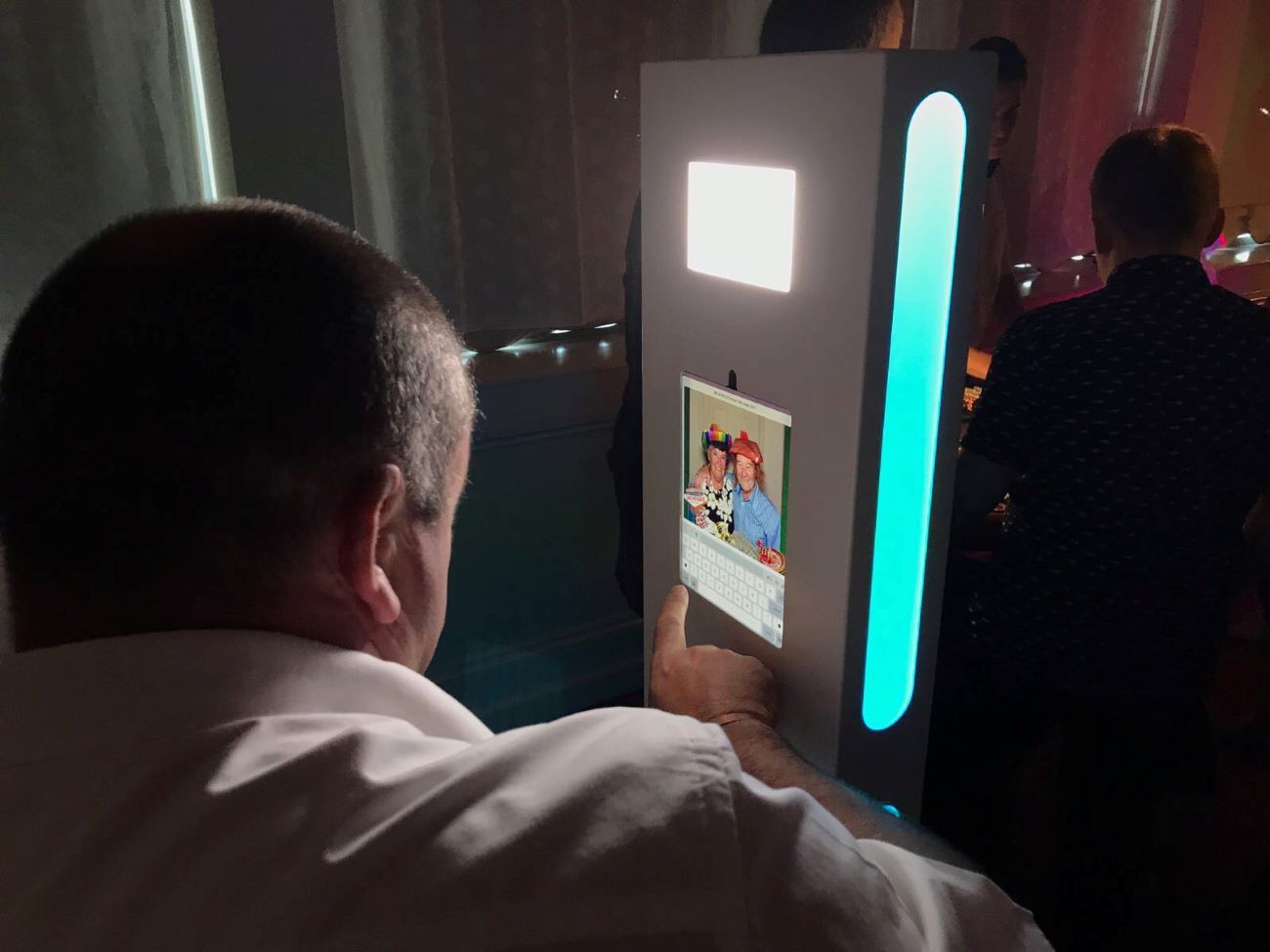 Guest tapping their email address into the selfie pod touchscreen to share a captured photo, with the fill light and LED strip illuminated