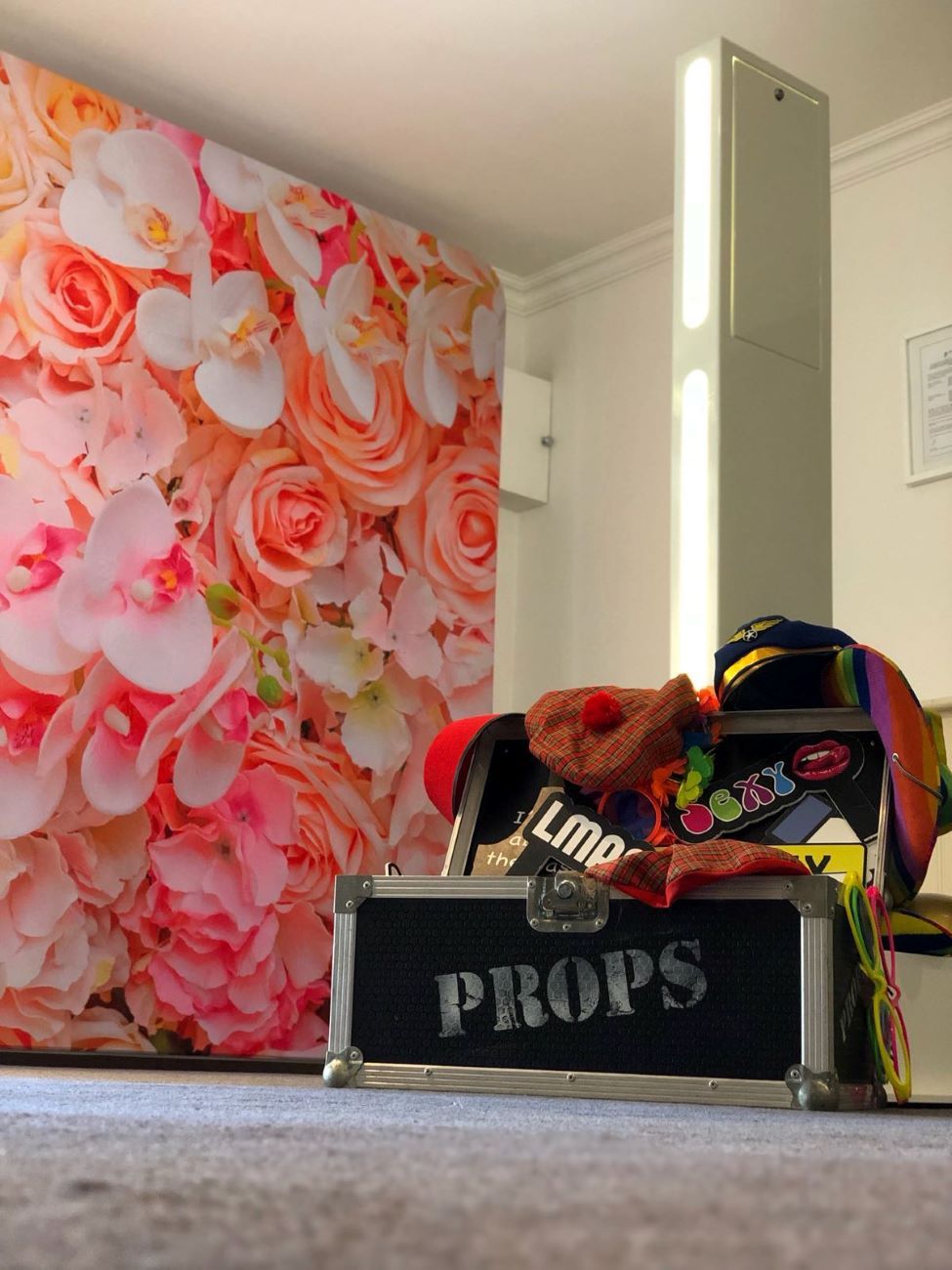 Close detail of the selfie pod's LED light strip alongside a pink floral wall backdrop, props case in the foreground