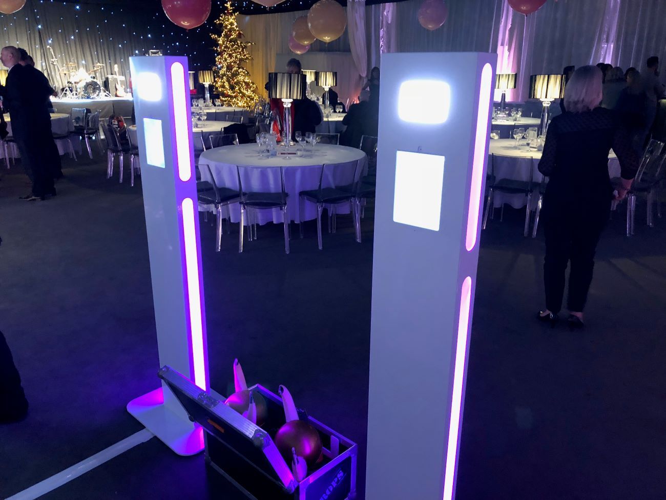 Two selfie pods set up side by side at a corporate Christmas dinner, Christmas tree and round dining tables in the background