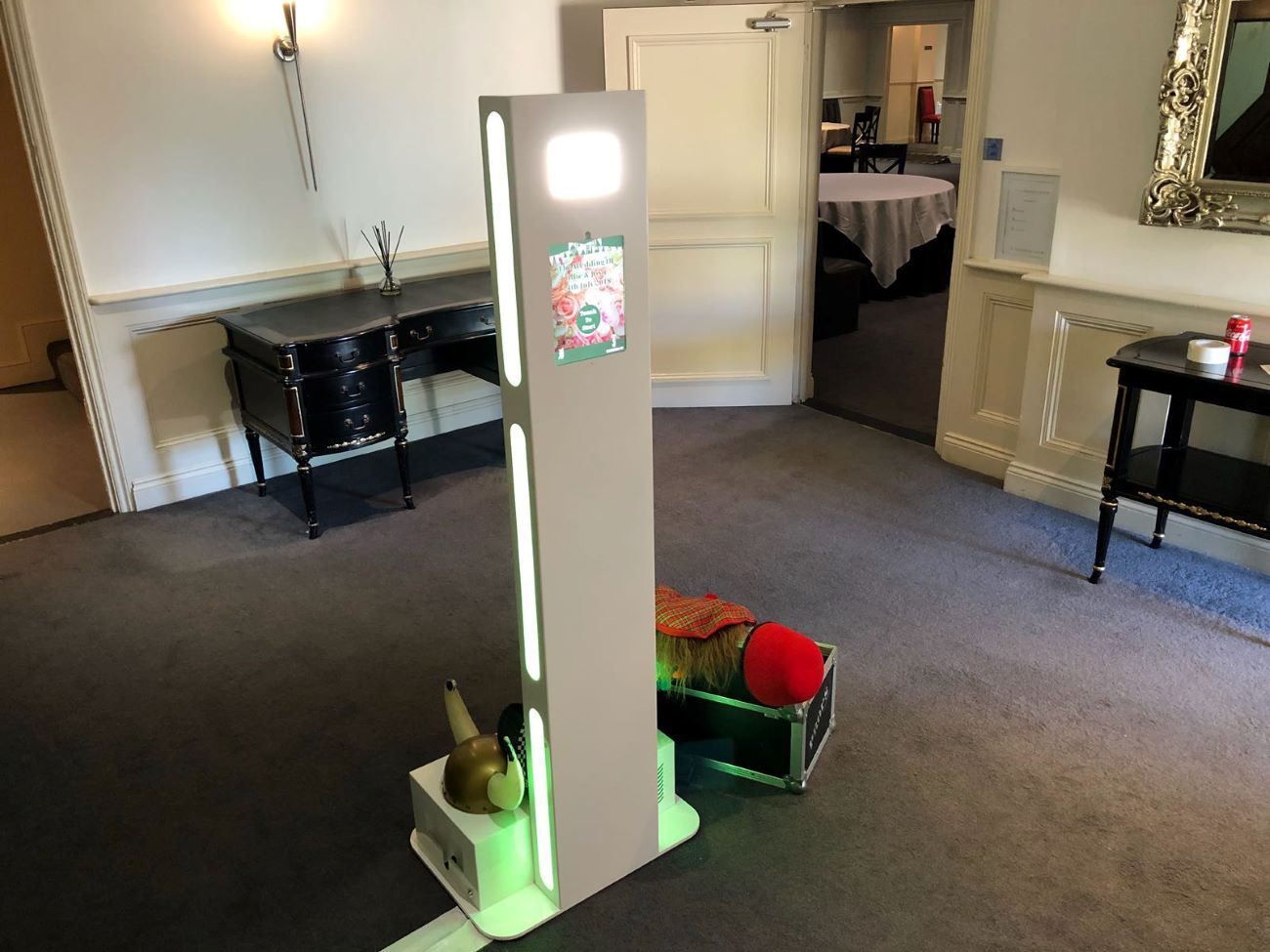 Selfie pod set up in a hotel wedding venue with a couple's poster on the front, props case beside it