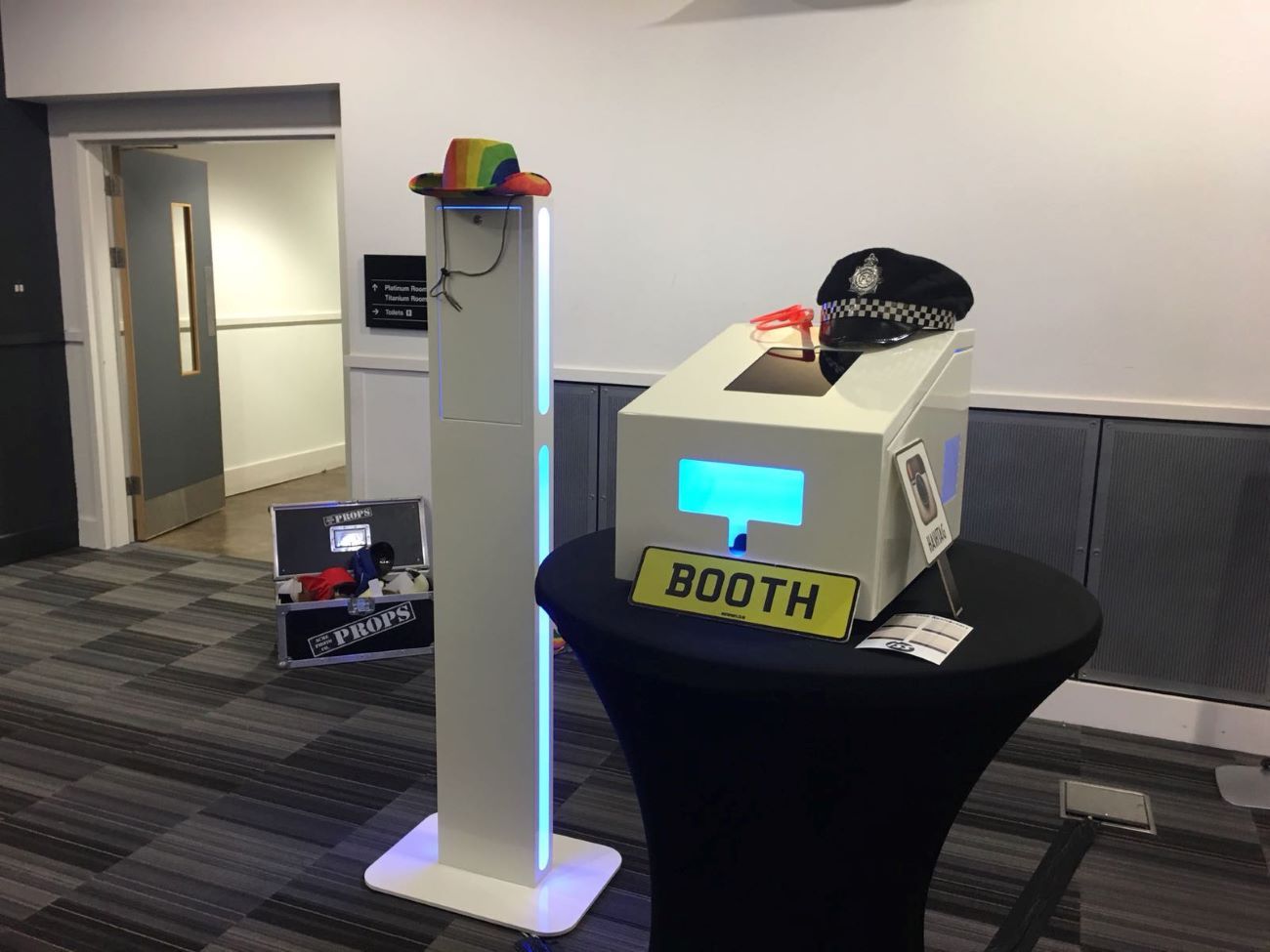 Selfie pod paired with an audio guestbook at a conference venue, props case behind and BOOTH licence-plate prop in the foreground