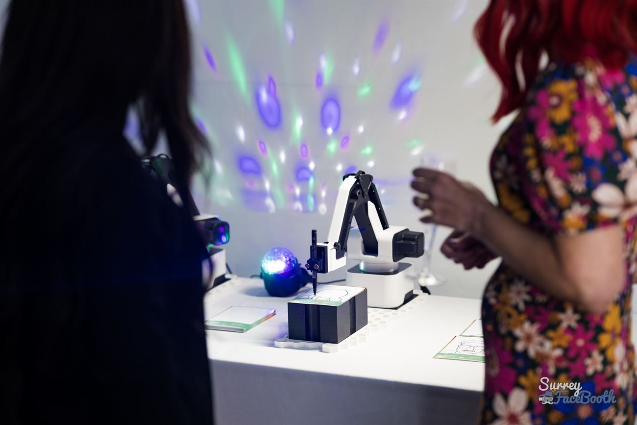 Two guests watching a sketch robot arm draw a portrait live at a party with disco lighting