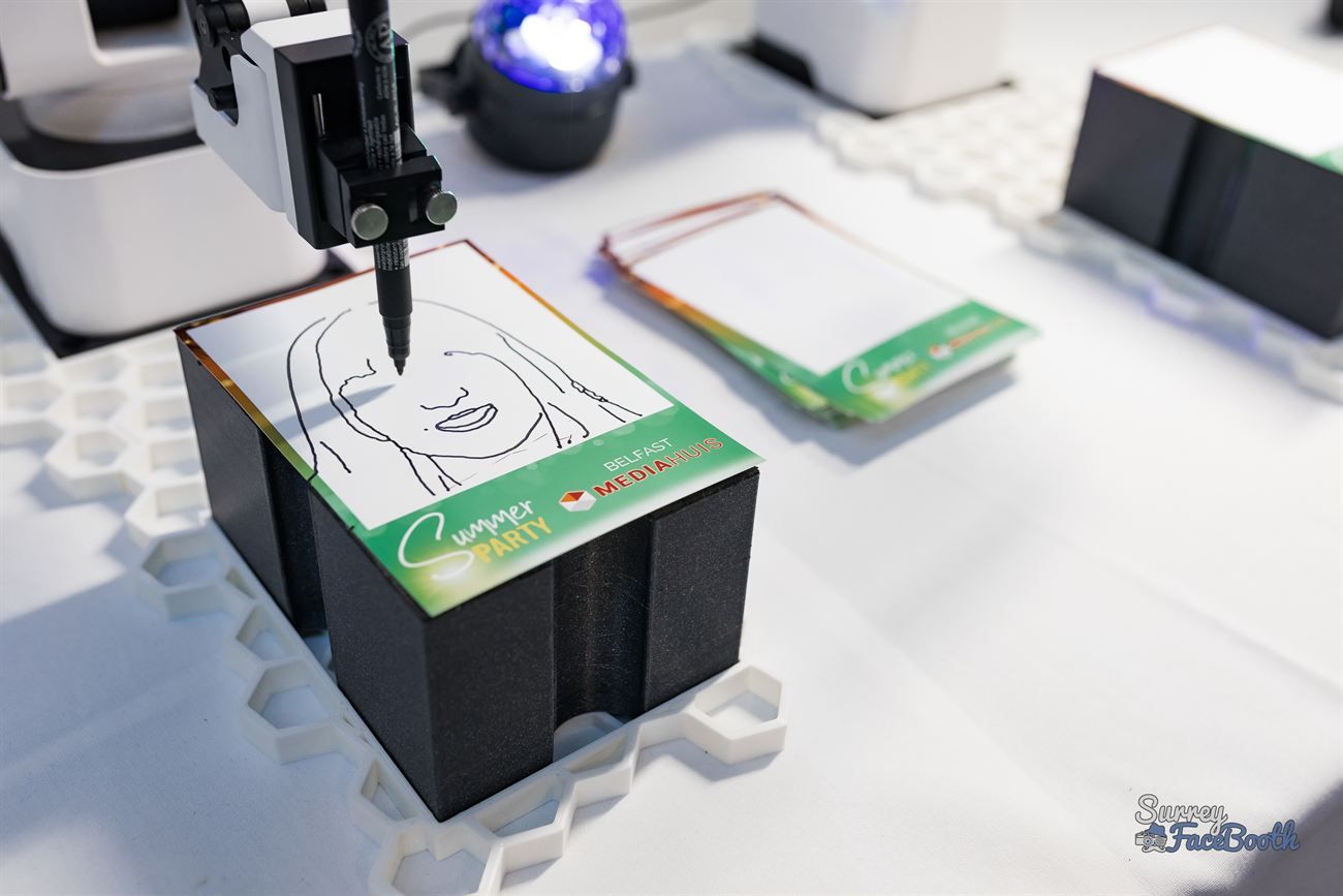 Close-up of a sketch robot's pen drawing a guest's portrait on a branded event card