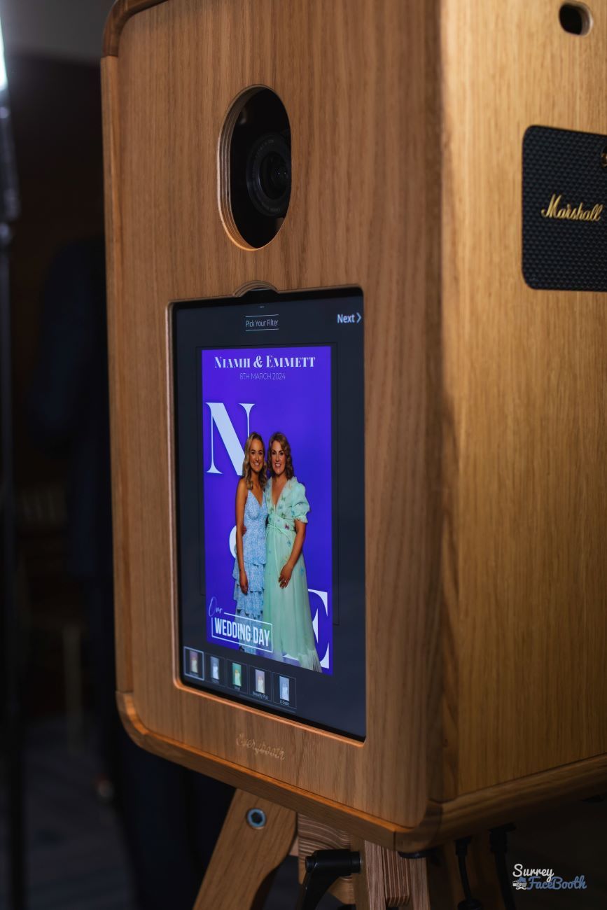 Vintage photo booth screen displaying a magazine-cover style branded overlay — two wedding guests with large 'N' and 'E' monogram letters and 'Our Wedding Day' caption