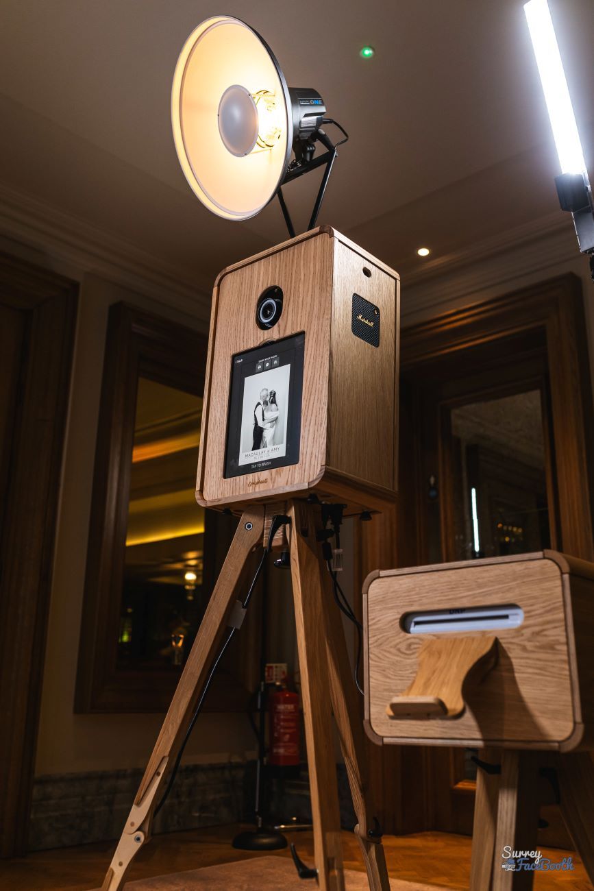 Vintage photo booth on its wooden tripod with the ring flash overhead, side cabinet housing the DNP dye-sublimation printer, set up in a chandelier-lit hotel ballroom for a wedding