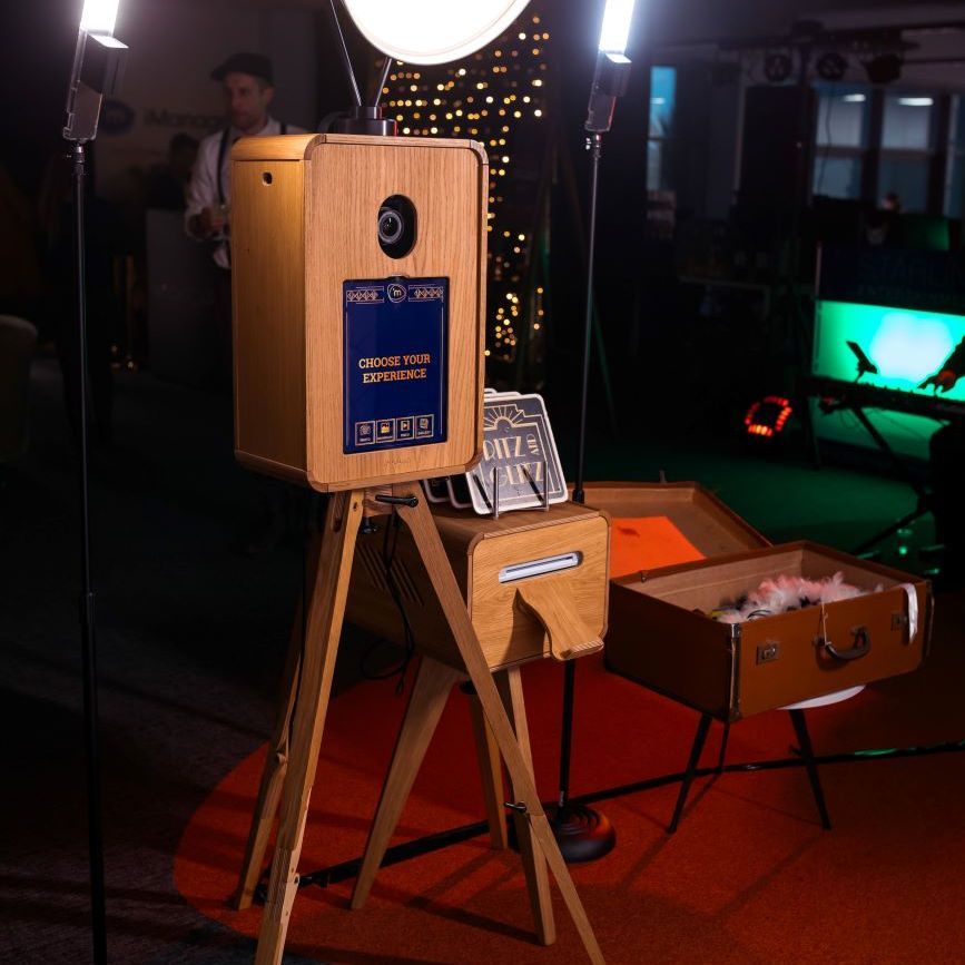 Vintage photo booth set up at a corporate Gatsby-themed event with the 'Choose Your Experience' selection screen, vintage suitcase prop box and ritz-style print frames alongside