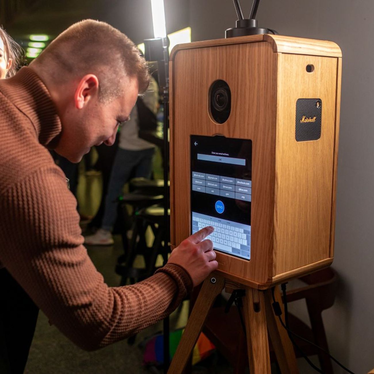 Guest at a corporate event tapping their email address into the vintage photo booth touchscreen to share their photo, with the booth's built-in Marshall speaker visible on the side