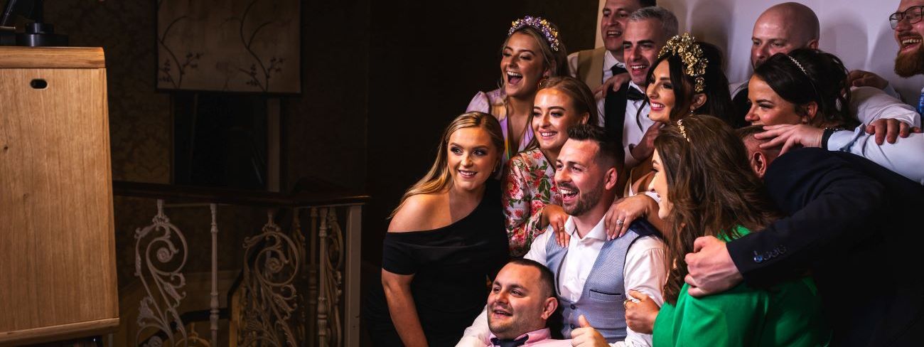 A large wedding group posing at a vintage wooden photo booth